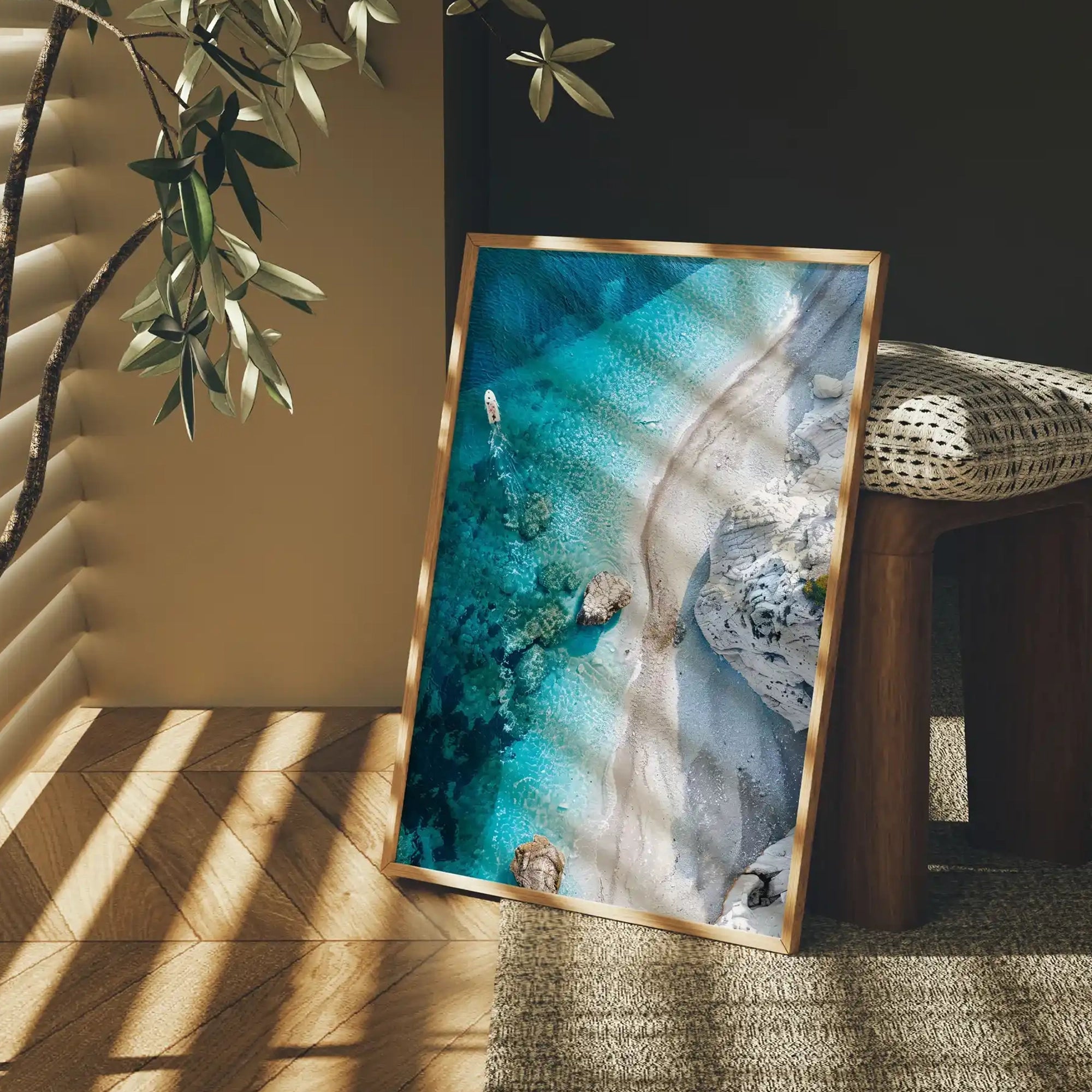 Aerial view of a turquoise beach with clear water and sandy shore, displayed as framed wall art in a modern interior with natural light.